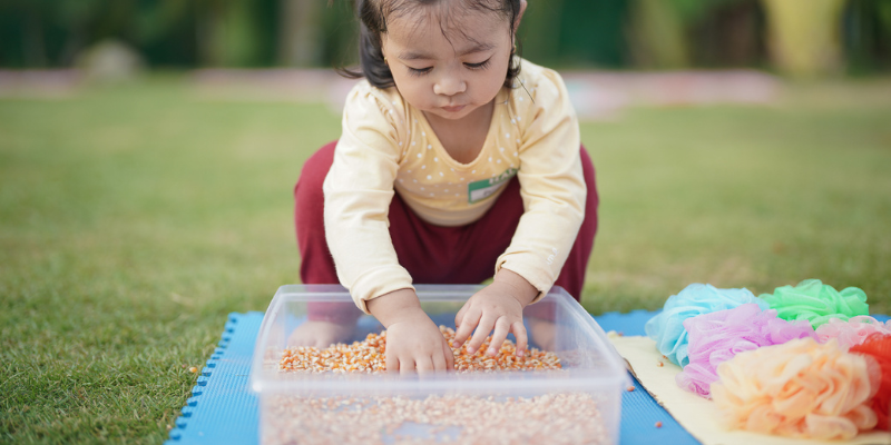 toddler playing in sensory bin outside